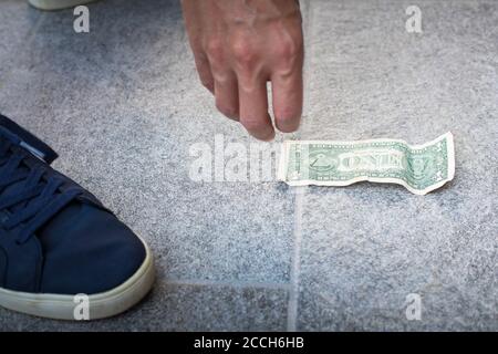 Mano maschio che raccoglie una fattura del dollaro dalla terra. Foto Stock
