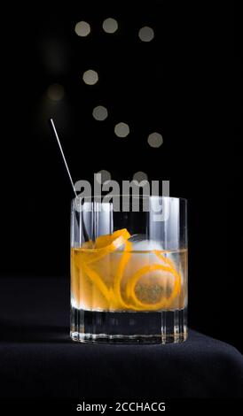 Elegante, moderna e sofisticata scena di un cocktail artigianale con guarnitura arancione in vetro roccioso isolato su sfondo nero con cerchi in bokeh grigio. Foto Stock
