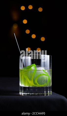 Sfondo nero con cerchi di bokeh arancioni caratterizzati da un'imbarcazione isolata cocktail con contorno di lime servito in un bicchiere di pietra Foto Stock
