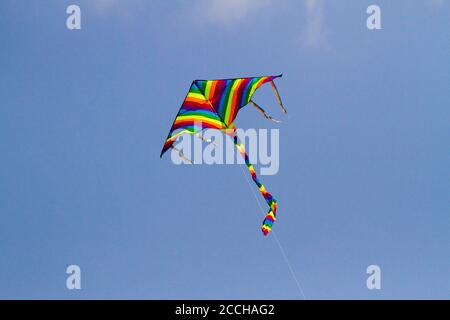 Il giocattolo preferito dai bambini si aquilano nelle giornate ventose in primavera, cielo blu e nuvole bianche. Un aquilone colorato oscilla nel vento. Foto Stock