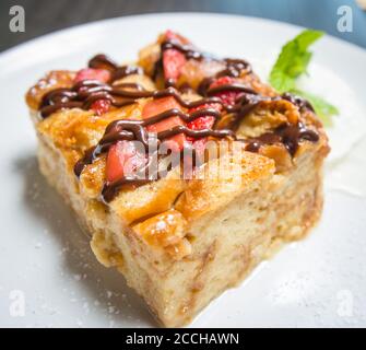 Una fetta di budino di pane condito con fragole e salsa al cioccolato, servita con panna montata Foto Stock