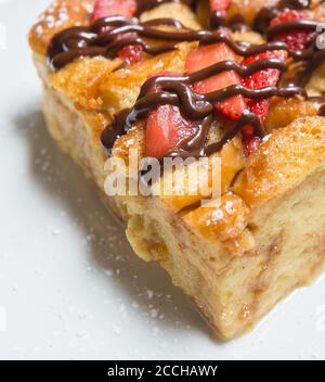 Primo piano di una fetta di budino di pane appena sfornato coperto in fragole e cioccolato Foto Stock