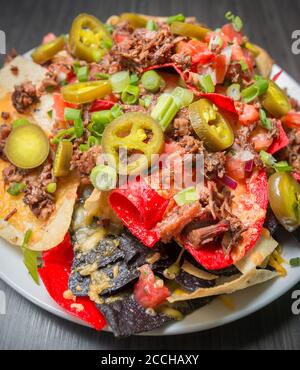 Closeup di un piatto di nachos di manzo fine bruciato con jalapeños e formaggio fuso su croccanti tortilla tricolore chips Foto Stock