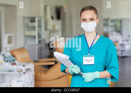 Ritratto di giovane infermiera in maschera e uniforme tenuta medica e guardando la macchina fotografica all'ospedale Foto Stock