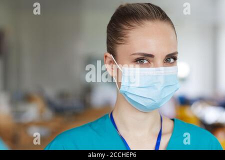 Ritratto di giovane bella infermiera indossando maschera protettiva e guardando alla telecamera Foto Stock