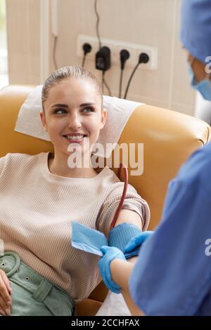 Giovane donna sdraiata sul divano e donando sangue mentre sorride al personale infermieristico Foto Stock