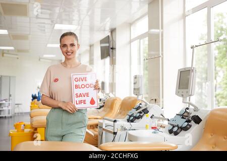 Ritratto di giovane donna che tiene il poster e sorridendo alla macchina fotografica mentre si è in piedi in laboratorio del sangue Foto Stock