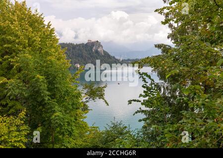 Iconico paesaggio sloveno, con un lontano castello accoccolato su un promontorio che si affaccia sul lago Bled, incorniciato da vegetazione verde Foto Stock