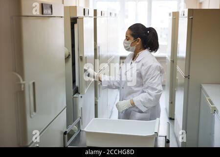 Medico femminile in camice bianco aprendo il frigorifero con sangue campioni in laboratorio Foto Stock