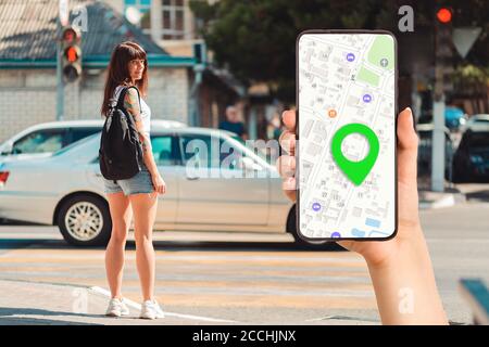 Una mano può contenere uno smartphone con un'app mappa online e una destinazione contrassegnata. Sullo sfondo, una donna si trova a un incrocio pedonale. Il concetto di Foto Stock