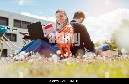 studente seduto in erba di fronte al palazzo universitario dando pollici in su Foto Stock