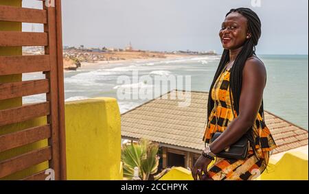 Donna africana vestita con colorate catene ghanaiane in piedi su un collina che domina la costa di Accra Foto Stock