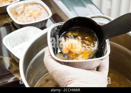 La mano sta servendo il dessert ashura con il mestolo nero, primo piano. Foto Stock