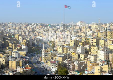 Amman, lo skyline della Giordania visto dalla cima della Cittadella. Città con costruzioni gialle e al Hashemi Street Avenue. Bandiera giordana sventolante. Foto Stock