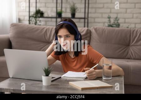 Una ragazza concentrata nelle cuffie studia sul computer portatile a casa Foto Stock