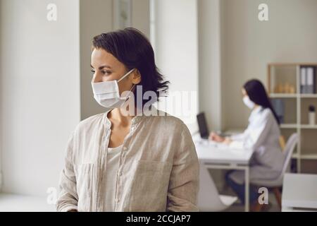 Paziente donna in maschera medica guardando la finestra in medico clinica durante la visita del medico Foto Stock