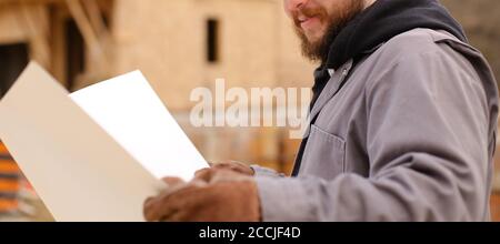 Banner di architetto maschile che tiene disegno piano di hause in cantiere. Foto Stock