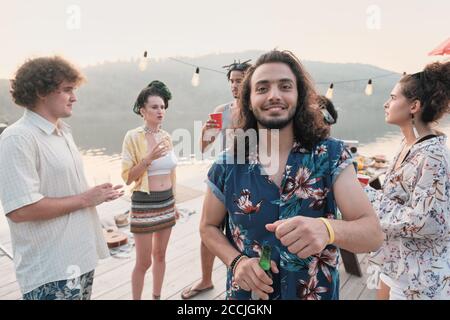 Ritratto del giovane bevendo birra e sorridendo alla macchina fotografica mentre si diverte in una festa Foto Stock