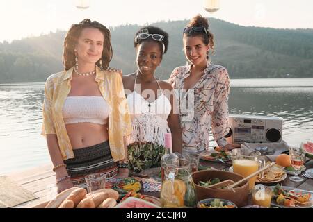 Ritratto di tre giovani donne che sorridono alla macchina fotografica mentre hanno una cena party all'aperto Foto Stock