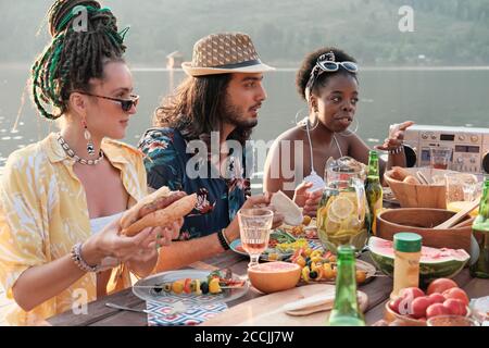 Gruppo di amici che si comunicano tra loro mentre si è seduti a. il tavolo durante il pranzo all'aperto Foto Stock