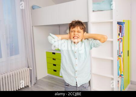 Piccolo ragazzo autistico con forte espressione negativa del viso che chiude le orecchie e denti di graniglia Foto Stock