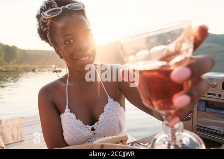Ritratto di giovane donna africana che sorride alla macchina fotografica e beve vino all'aria fresca Foto Stock