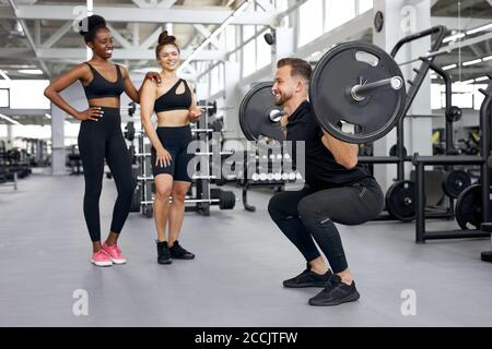 l'addestratore caucasico sta insegnando gli esercizi con i pesi alle donne attraenti differenti, dumbbell, corso di sollevamento del barbell per aumentare i muscoli del corpo per essere stro Foto Stock