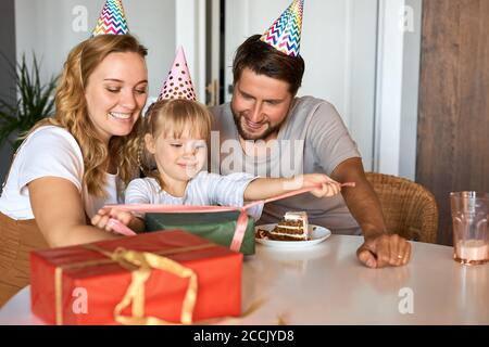 bambina caucasica in attesa di ricevere, disimballaggio doni dai genitori. adorabile ragazza felice celebrare il compleanno a casa con la famiglia Foto Stock