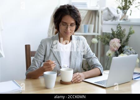 Felice giovane donna d'affari aggiungendo zucchero raffinato alla tazza di caffè. Foto Stock