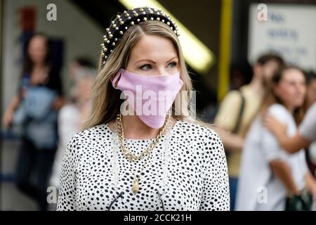 Giovane donna dal look elegante che indossa una copertura per il viso di un designer su una strada trafficata, Londra, Regno Unito Foto Stock