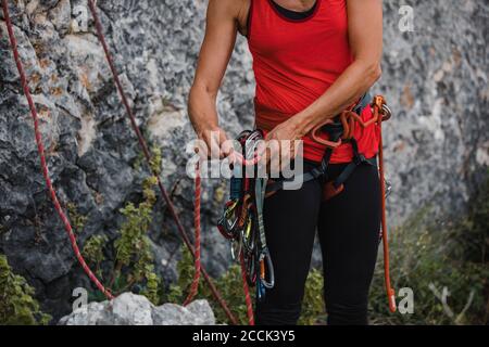 Donna che regola le corde mentre si prepara per l'arrampicata su roccia Foto Stock