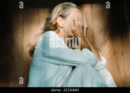 Donna anziana triste seduta da sola con le mani che coprono il viso Foto Stock