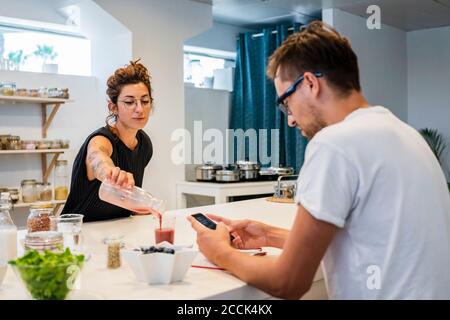 Studentessa che serve succo per l'uomo utilizzando smartphone in scuola di cucina Foto Stock