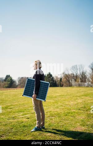 Imprenditore maschile che tiene pannello solare mentre si guarda lontano al parco il giorno di sole Foto Stock