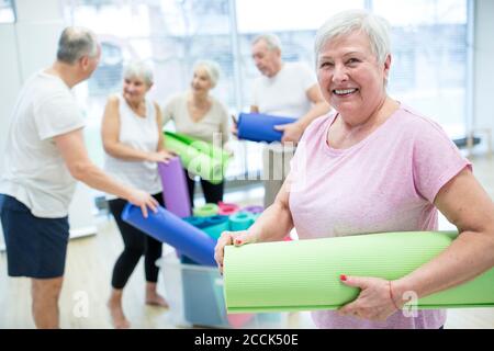 Donna anziana felice che tiene il tappeto di yoga dopo la lezione Foto Stock