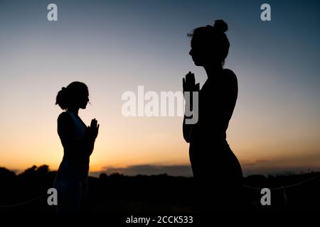 Silhouette di donne in posizione di preghiera all'aperto Foto Stock