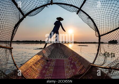 Myanmar, stato di Shan, Silhouette di pescatore tradizionale Intha in barca sul lago di Inle al tramonto Foto Stock