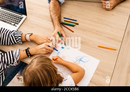 Mani di genitori che dipingono con la figlia su carta per cena tavolo a casa Foto Stock