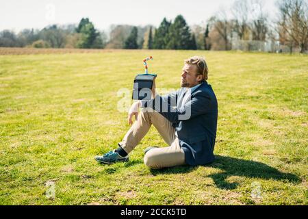 Uomo d'affari che analizza il braccio del robot durante la ricarica con il pannello solare portatile al parco il giorno di sole Foto Stock