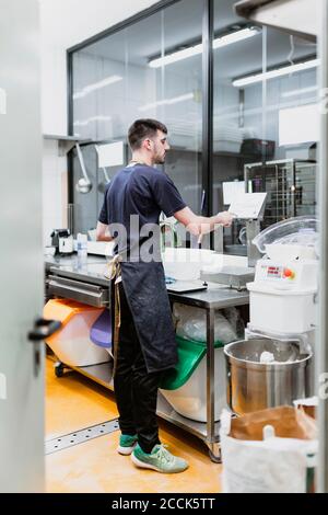 Giovane panettiere che lavora al banco della cucina in panetteria Foto Stock