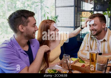 piccolo adesivo sulla fronte. amici che si divertono nel ristorante, caucasici giovani che giocano un hedbanz gioco, ridere Foto Stock