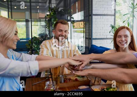 un gruppo caucasico di migliori amici si è unito a mani seduti al tavolo del caffè, giovani felici in riunione, unità e sostegno. concetto di amicizia Foto Stock