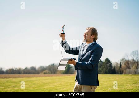 Ingegnere che analizza il braccio del robot durante la ricarica con il pannello solare portatile contro il cielo limpido nella giornata di sole Foto Stock