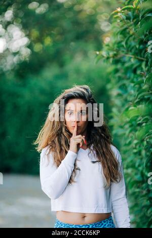 Giovane donna con un dito sulle labbra in piedi da piante in parcheggio Foto Stock