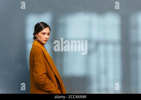 Donna che indossa un cappotto invernale giallo mentre si trova accanto alla parete grigia Foto Stock