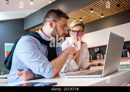 Professionisti di fiducia di sesso maschile e femminile pianificazione della strategia mentre discutono sopra computer portatile in ufficio Foto Stock