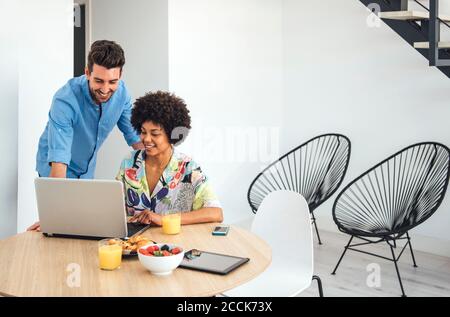 Felice coppia che usa un computer portatile al tavolo da pranzo in un attico moderno Foto Stock