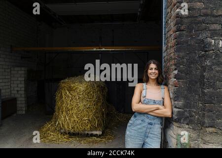 Ritratto di giovane donna sorridente appoggiata contro muro di mattoni a. un fienile in una fattoria Foto Stock