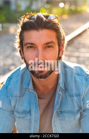 Primo piano di un uomo bearded che indossa occhiali da sole sulla testa mentre si siede in città Foto Stock