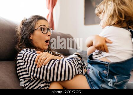 Felice madre che gioca con la figlia mentre si siede sul divano a. casa Foto Stock